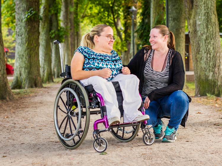 Porträt einer behinderten Frau im Rollstuhl mit Assistent im Park